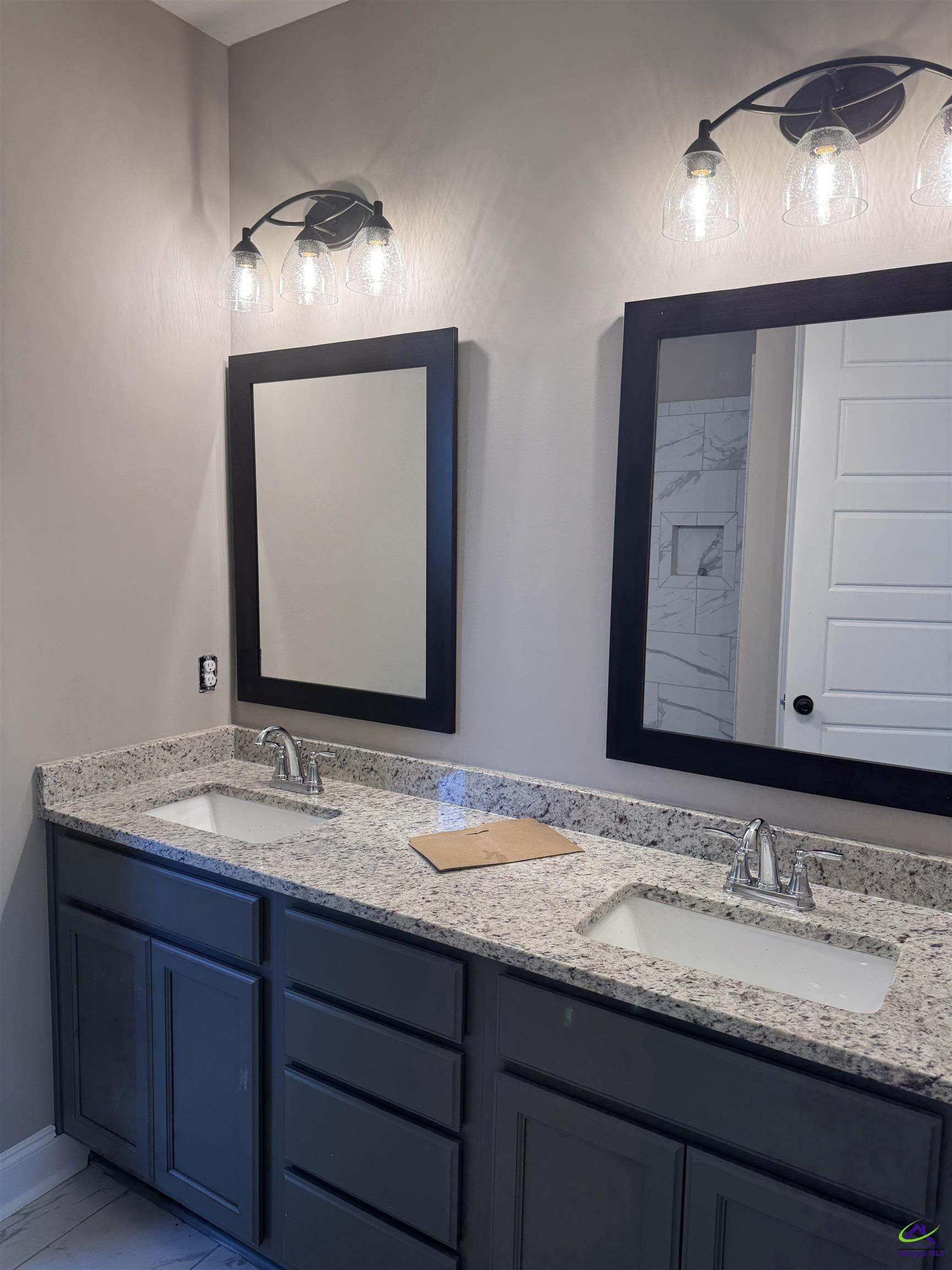 Bathroom with a double-sink granite vanity, dark blue cabinets, black-framed mirrors, and glass pendant lights.
