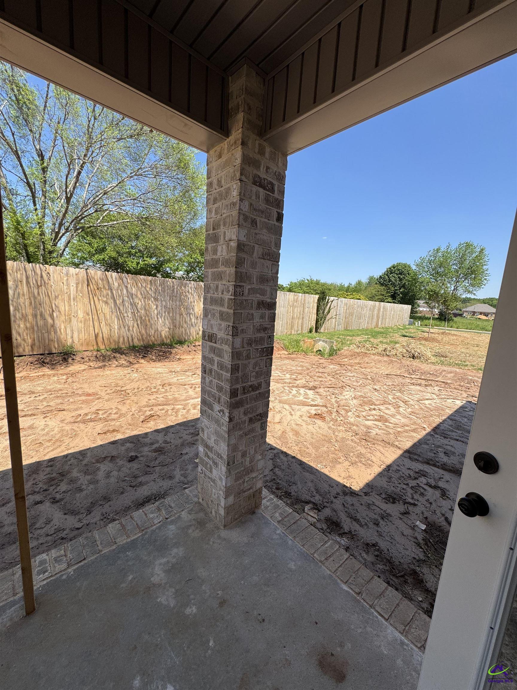 Covered patio with a brick column and concrete floor overlooking a fenced, mostly bare backyard.