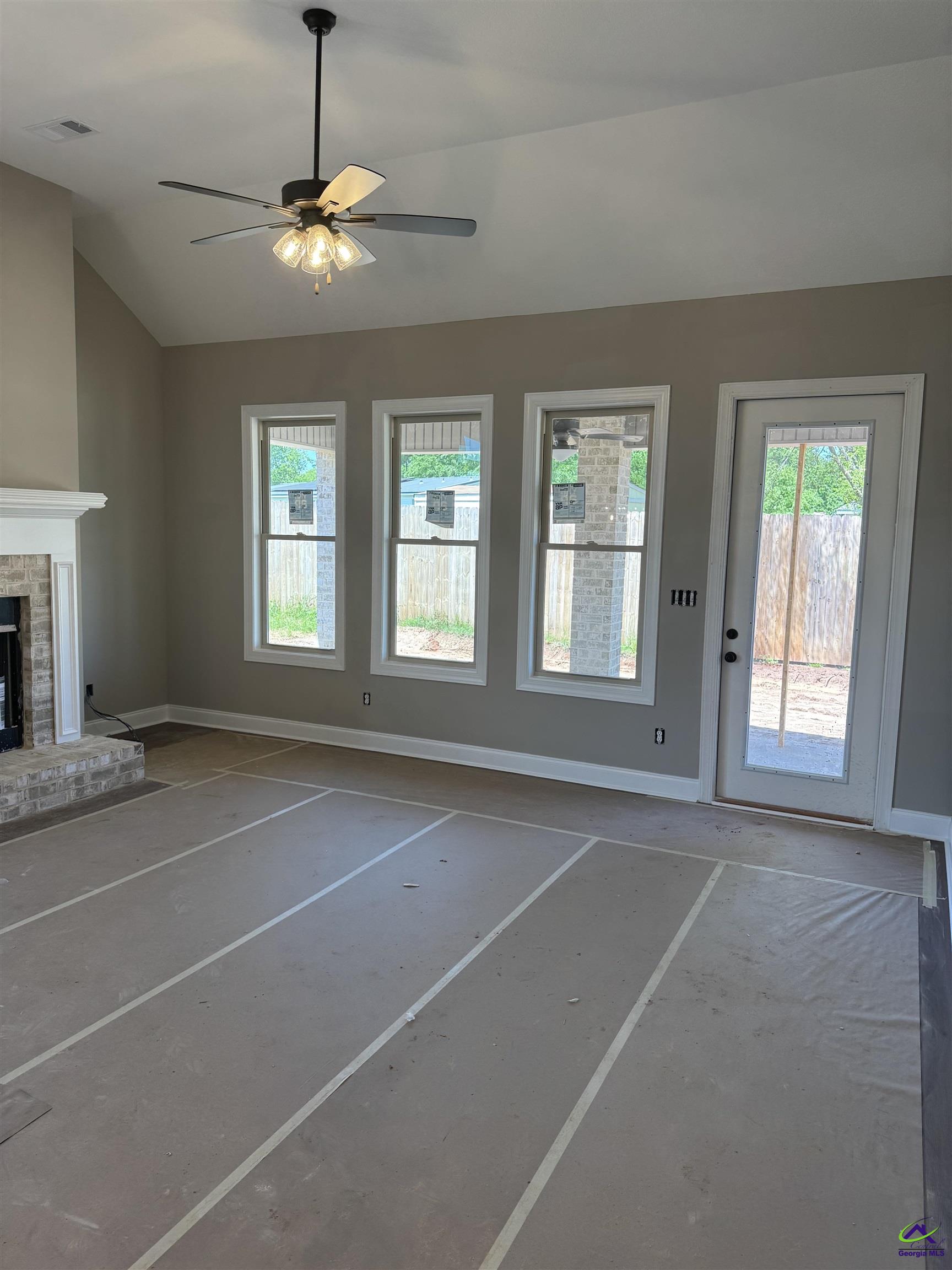 Living room with a brick fireplace, high ceiling, and windows beside a glass-panel door.