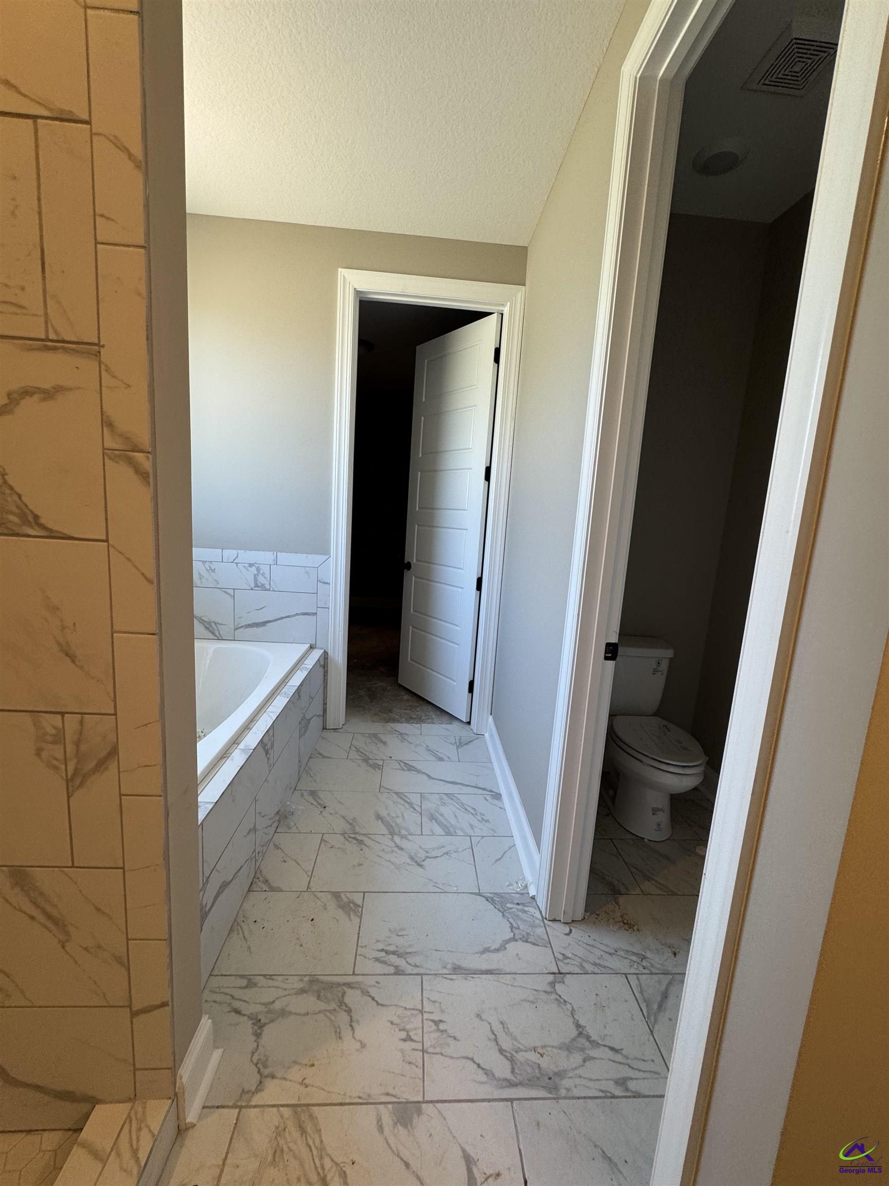 Bathroom with marble-look tile flooring, a bathtub, and a separate toilet room.