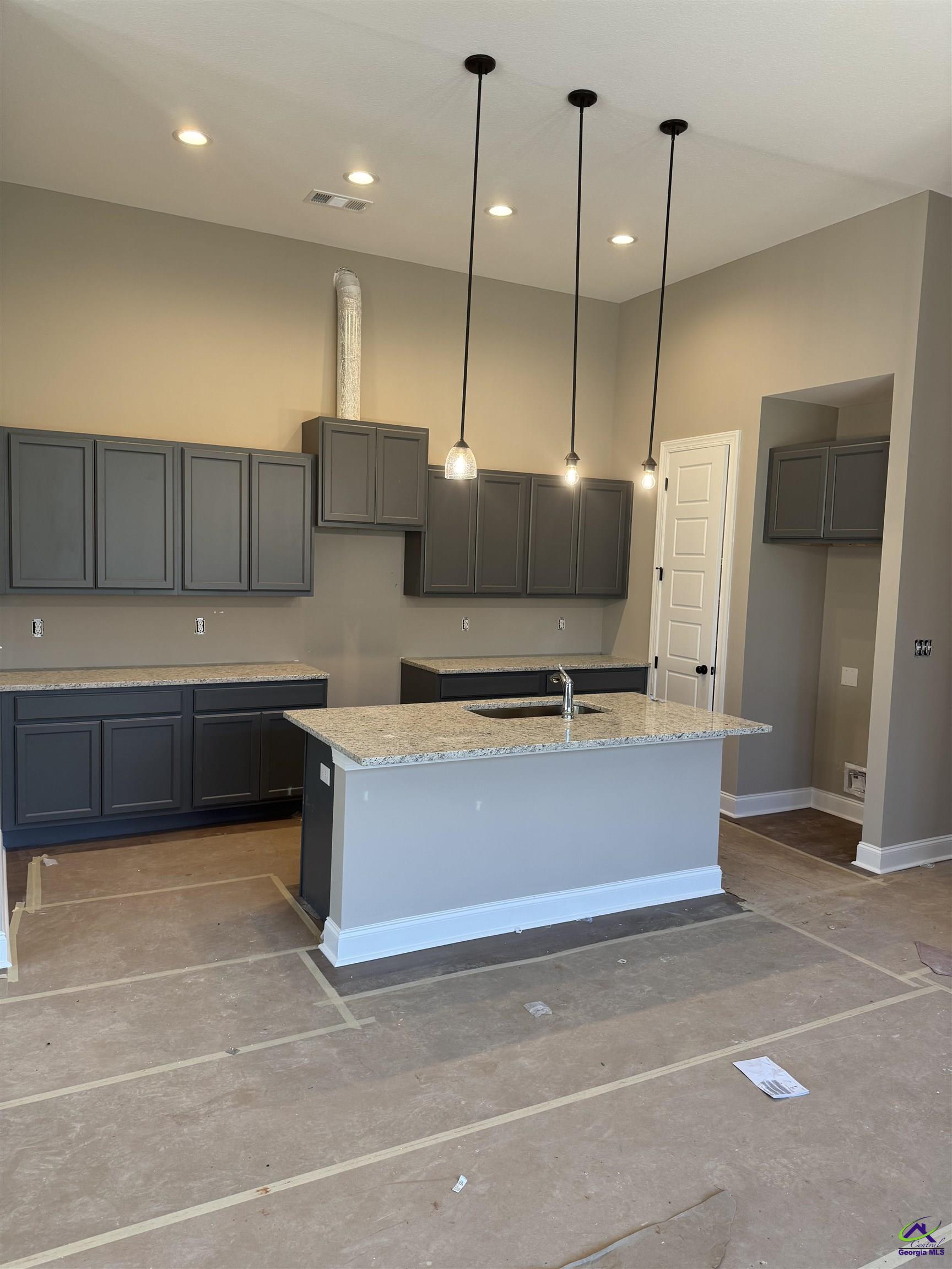Unfinished kitchen with dark gray cabinets, granite counters, a sink island, and pendant lights.