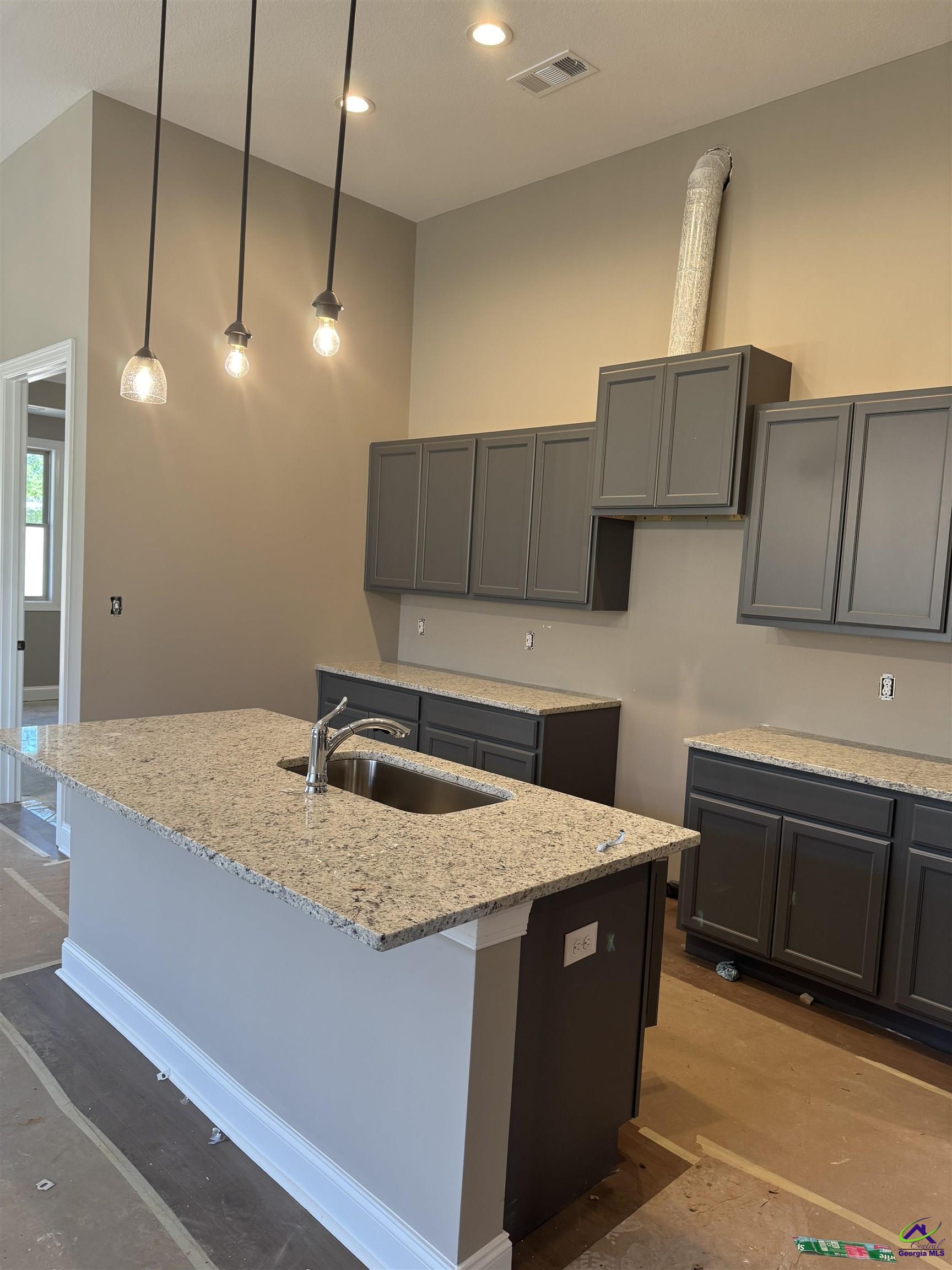Kitchen with granite island and sink, dark cabinetry, pendant lights, and unfinished flooring.