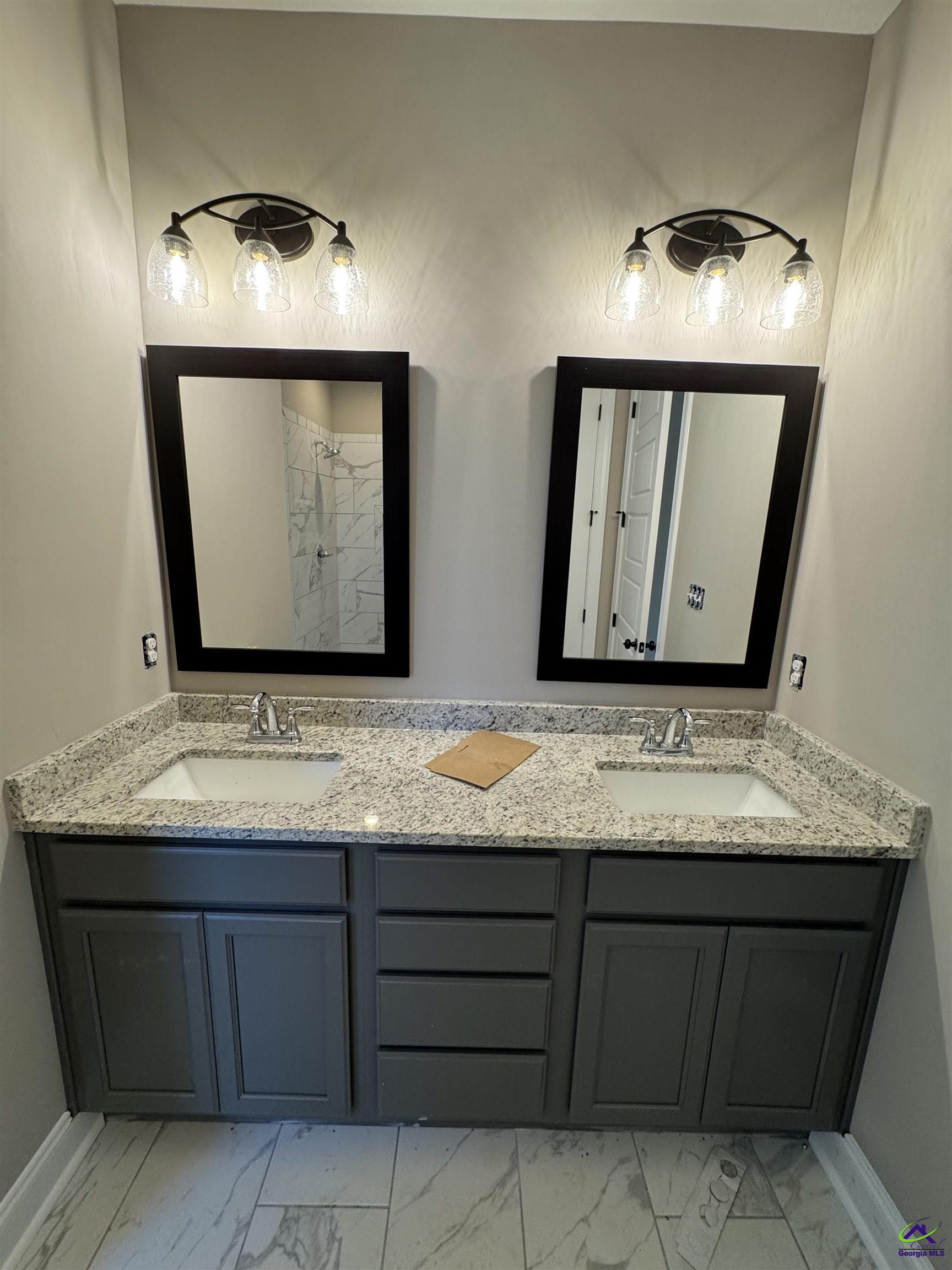 Bathroom double vanity with dark gray cabinets, granite countertop, and black-framed mirrors.