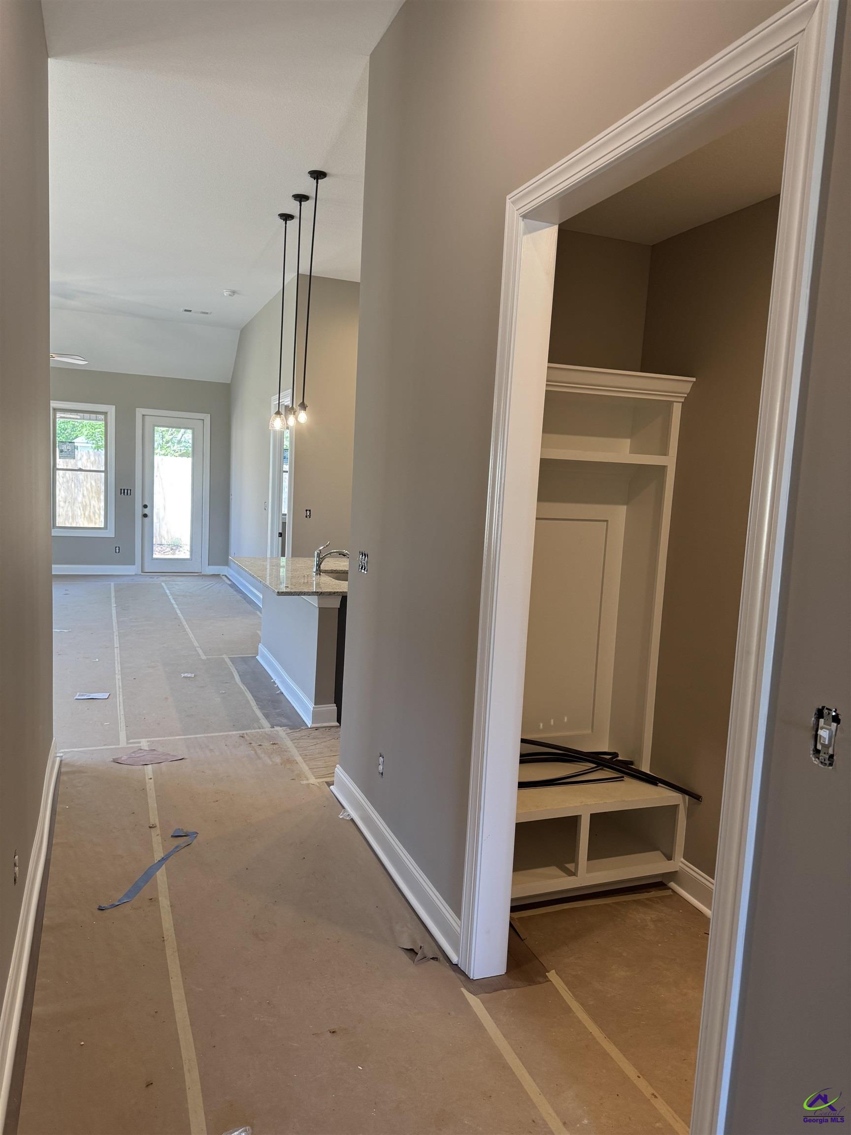 Hallway opening to a bright living area, with a kitchen peninsula and built-in shelving and cubbies.