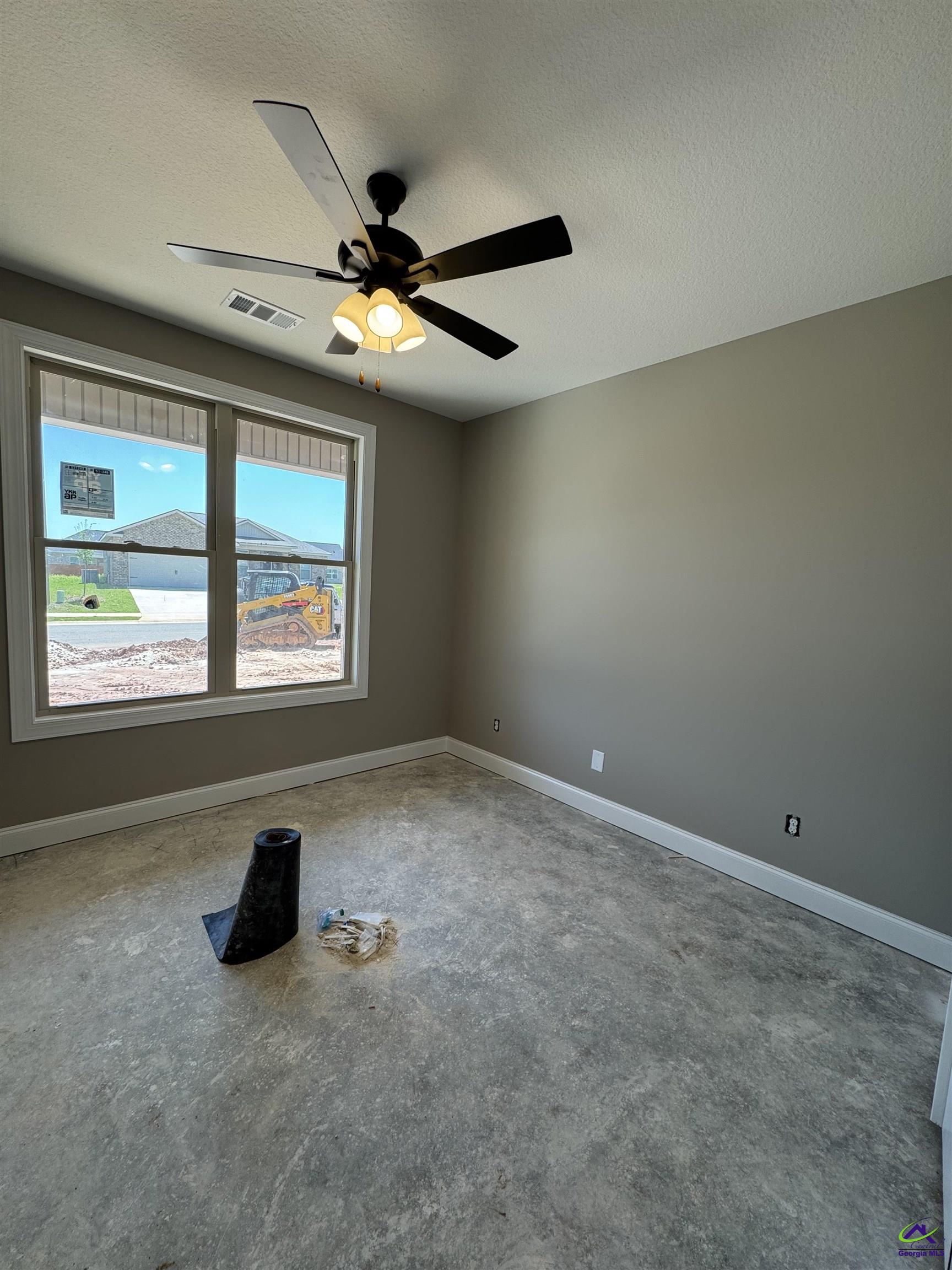 Unfinished room with a concrete floor, ceiling fan, and large window overlooking construction.