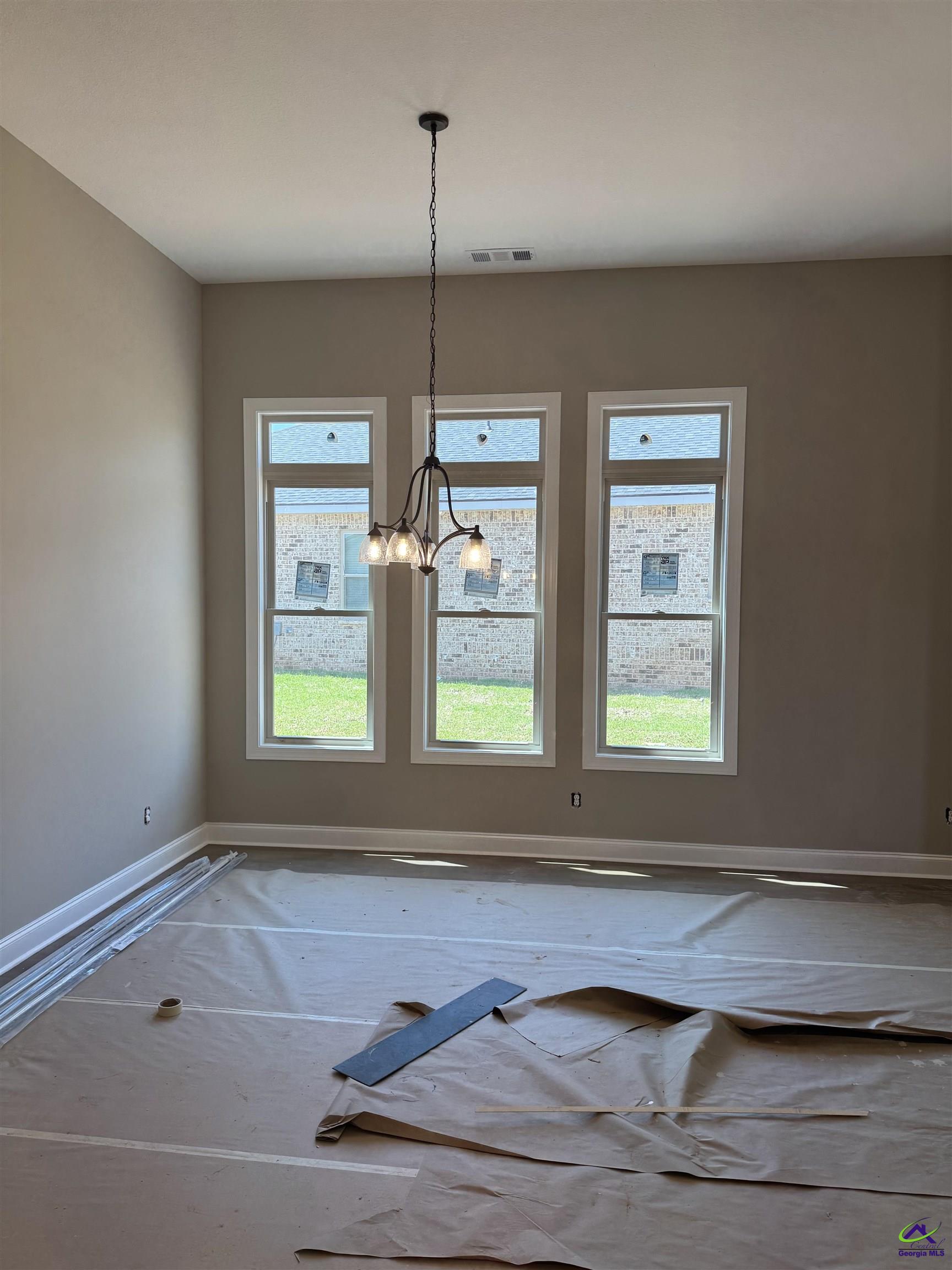 Unfinished dining room with three tall windows, a chandelier, and protective floor covering.