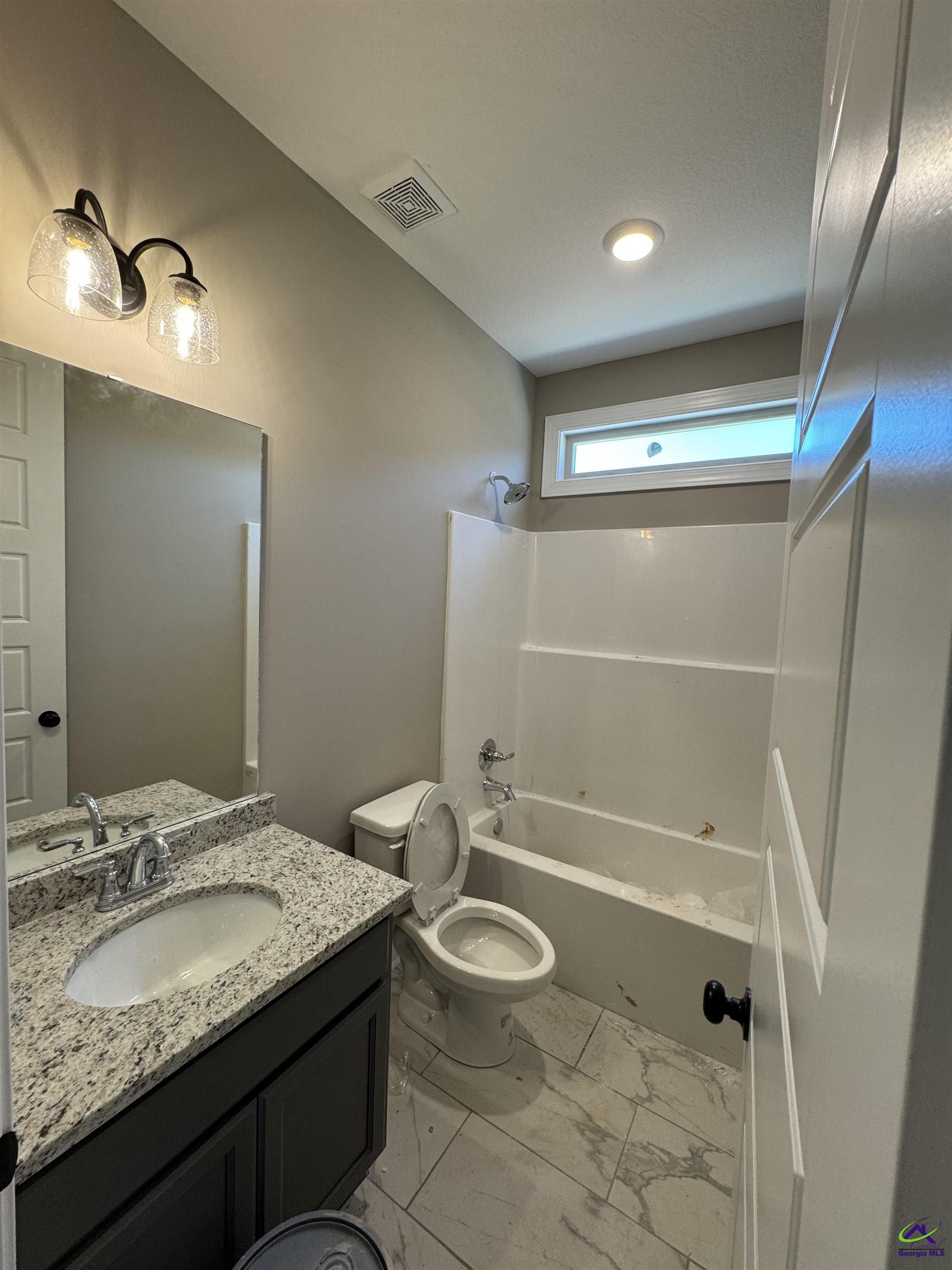 Bathroom with granite vanity, toilet, and tub-shower beneath a narrow window.