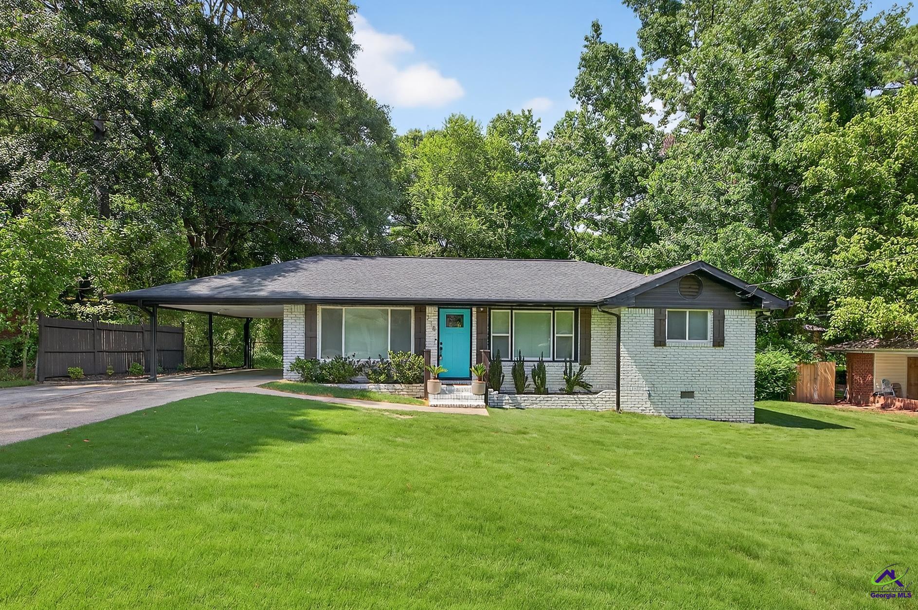 Single-story brick home with a turquoise front door, attached carport, and tree-lined lawn.