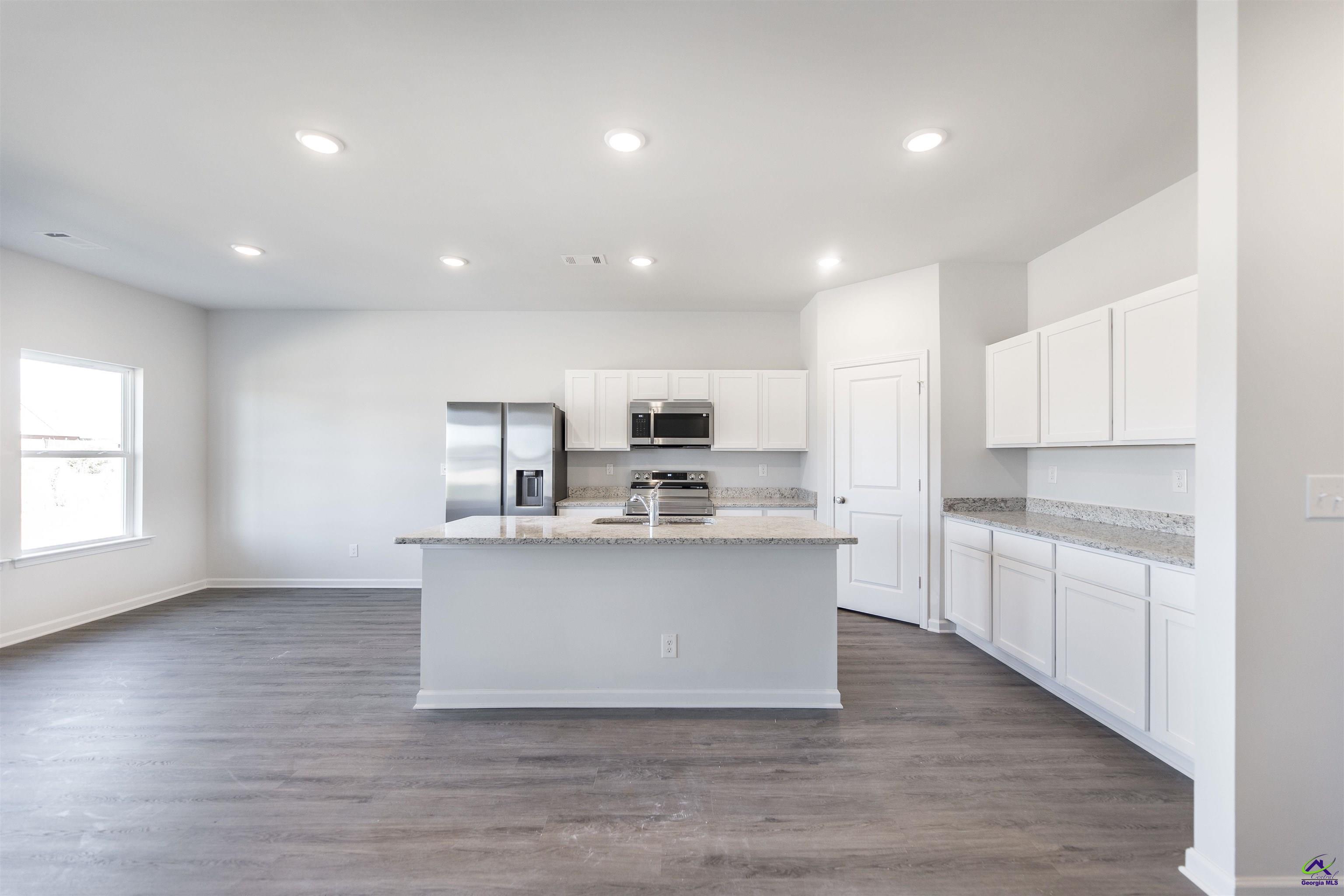 Vacant kitchen with white cabinets, stainless steel appliances, and a large granite-topped island.