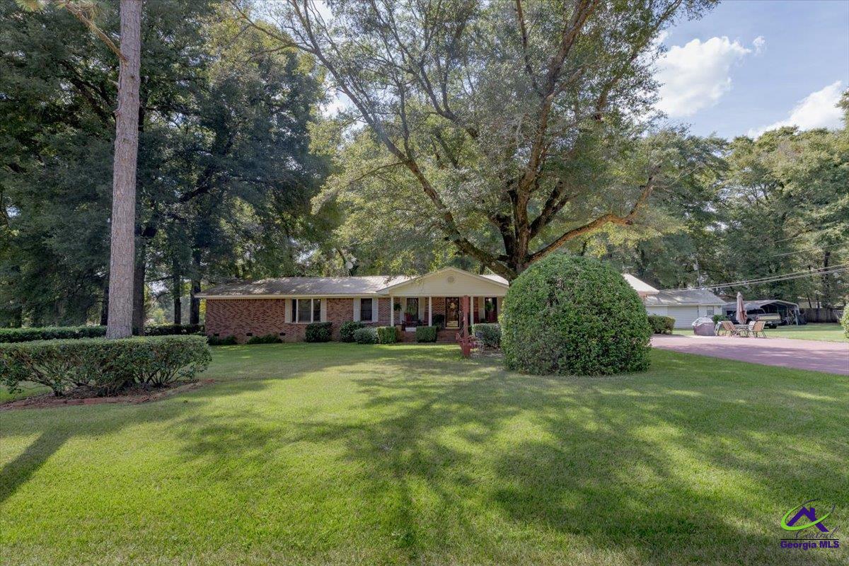 Brick ranch house set behind a broad lawn, shaded by mature trees.
