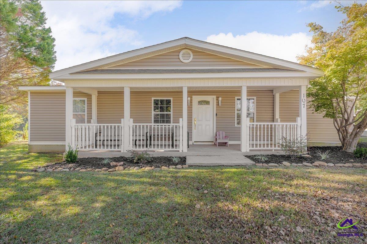 Single-story home with a broad covered front porch, white railings, and beige siding.