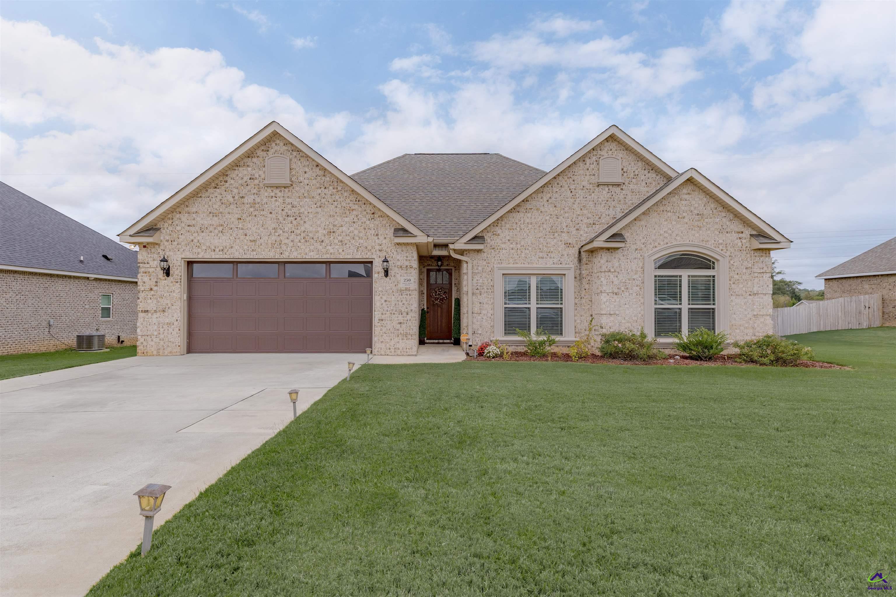 Light brick home with a two-car garage, broad driveway, and neatly maintained front lawn.