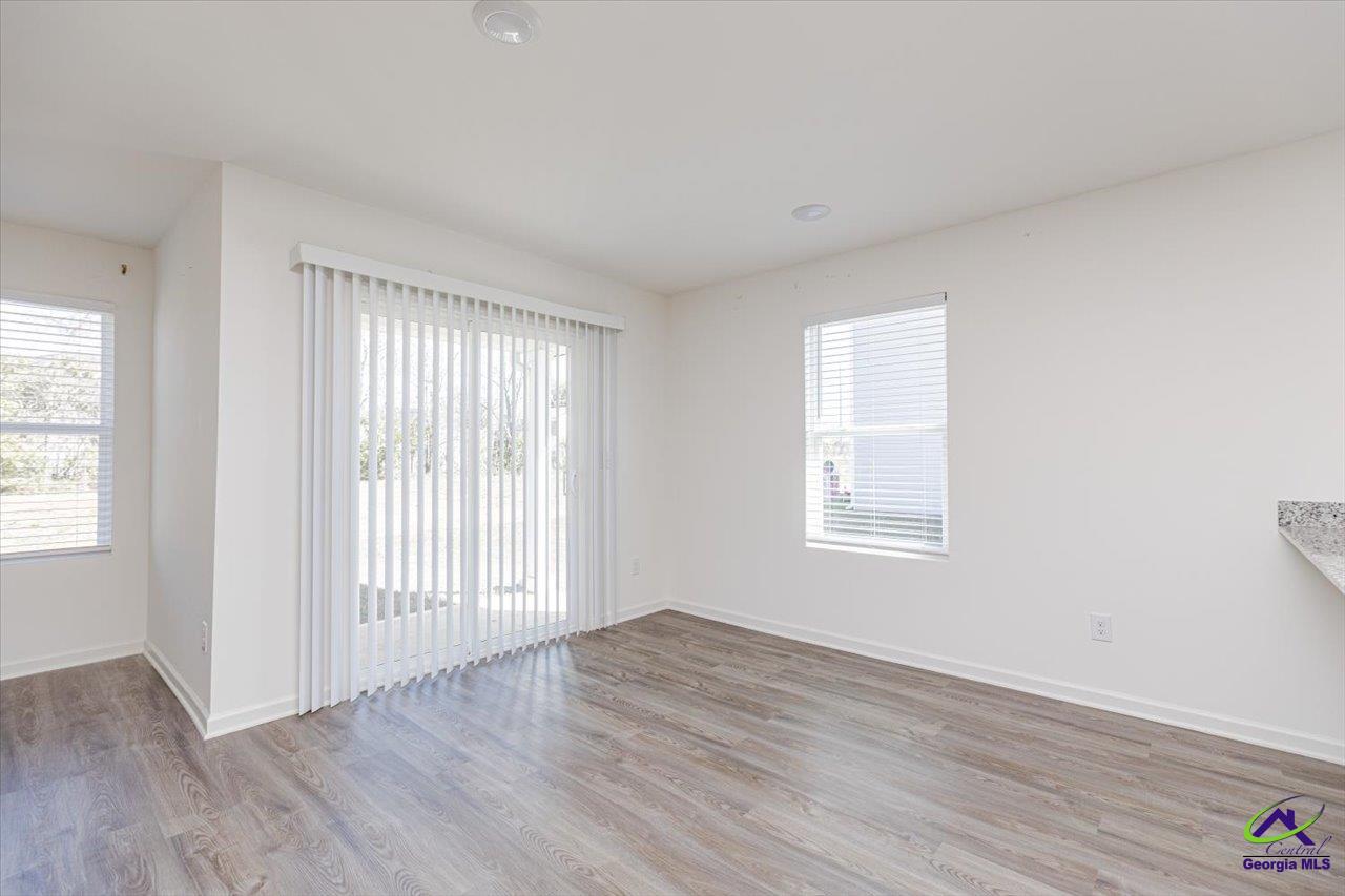 Empty room with plank flooring, a sliding glass door, and windows with blinds.