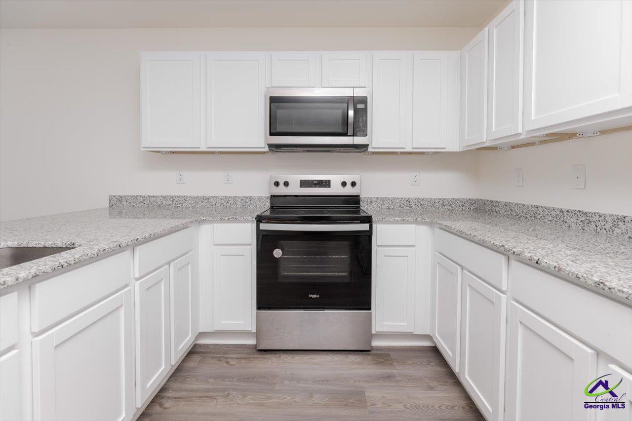 Kitchen with white cabinets, granite countertops, stainless steel appliances, and gray wood-look flooring.