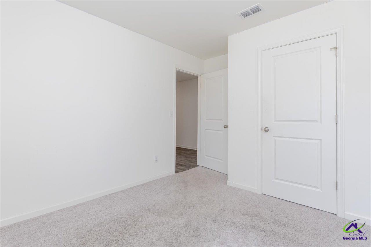 Empty carpeted room with white walls, a closed door, and an open doorway.