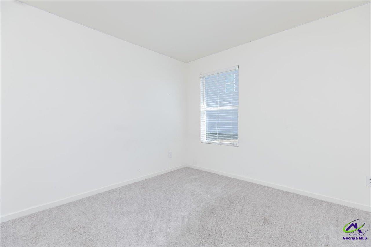 Empty carpeted bedroom with white walls and a window fitted with blinds.