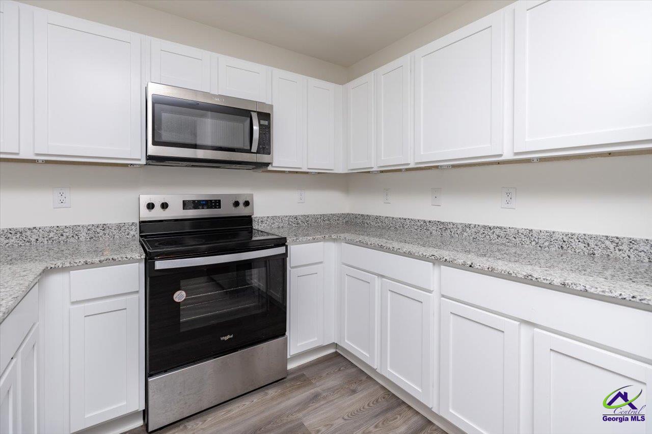 Kitchen with white cabinets, speckled granite counters, and a black-and-stainless range beneath a microwave.