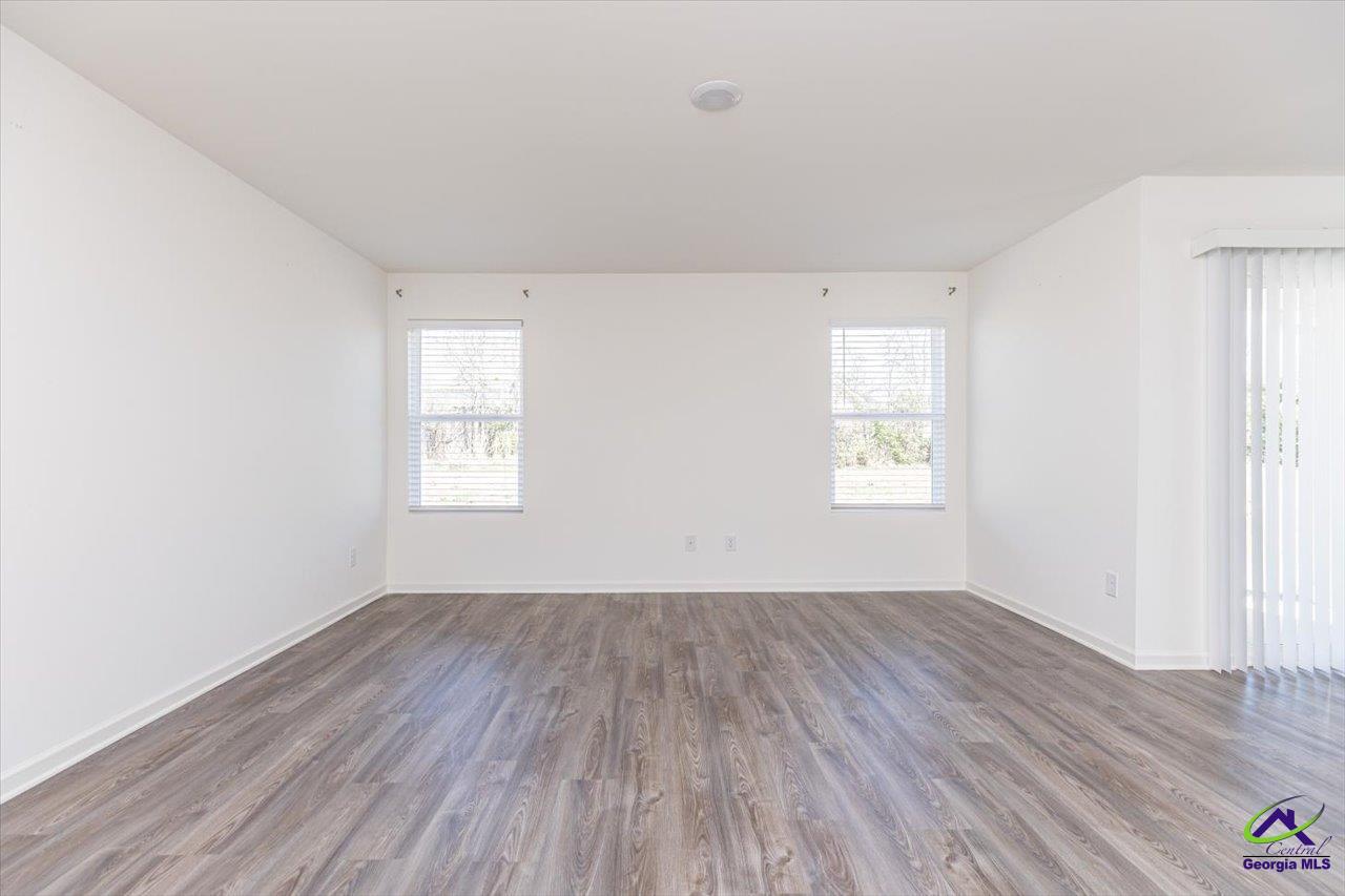 Empty living room with wood-look flooring, two windows, and vertical blinds over a sliding glass door.