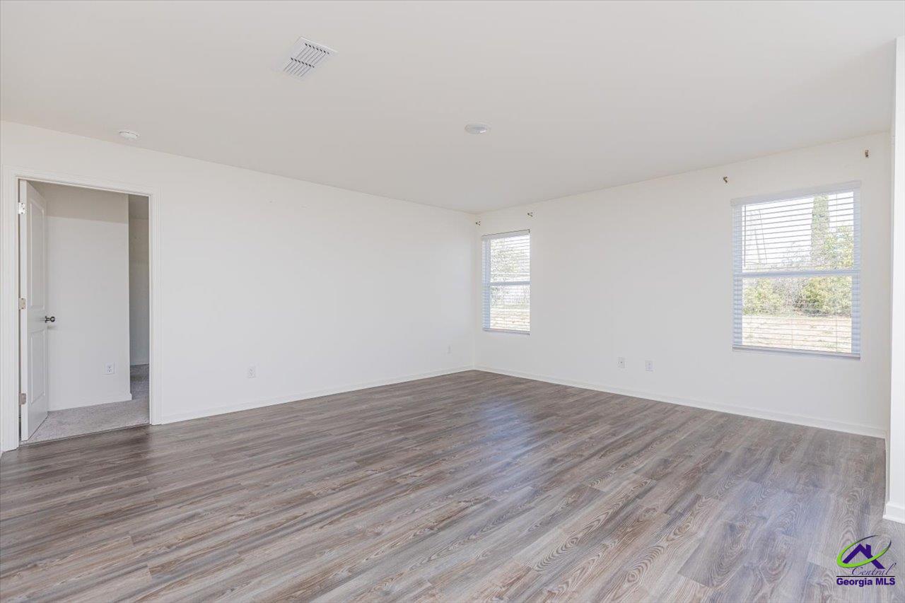 Empty room with gray wood-look flooring, white walls, and two windows.