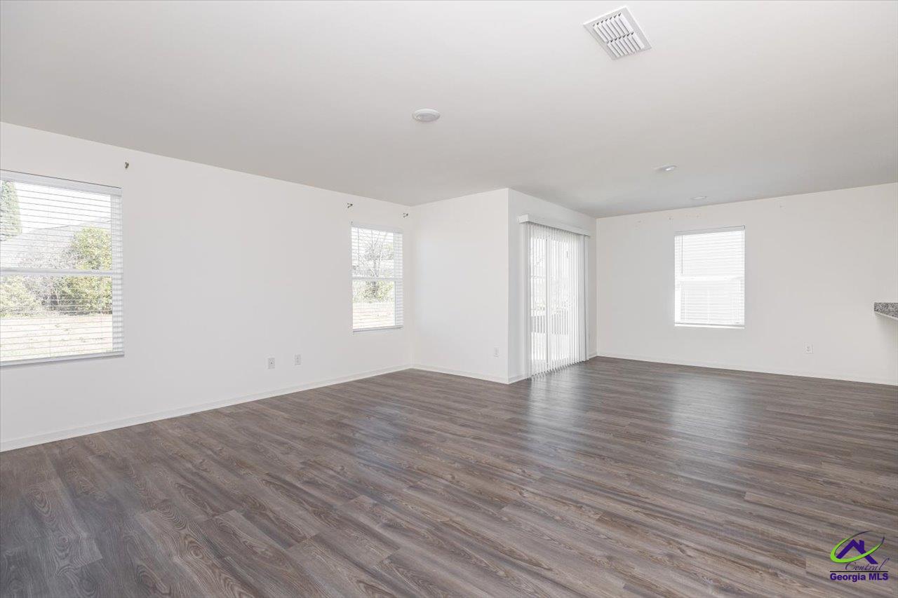 Empty living room with dark wood-look floors, several windows, and a sliding glass door.