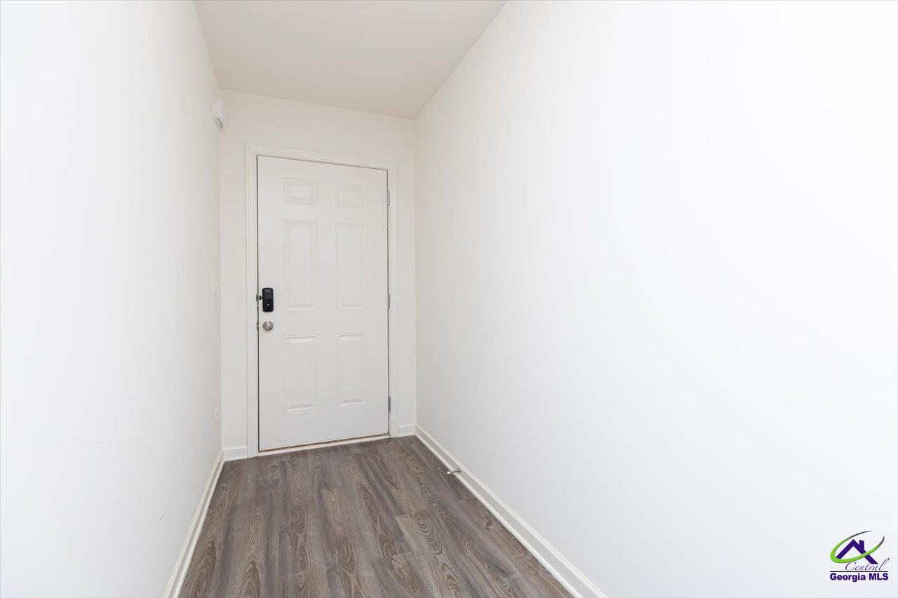 Empty entry hall with wood-look flooring and a white front door with keypad lock.