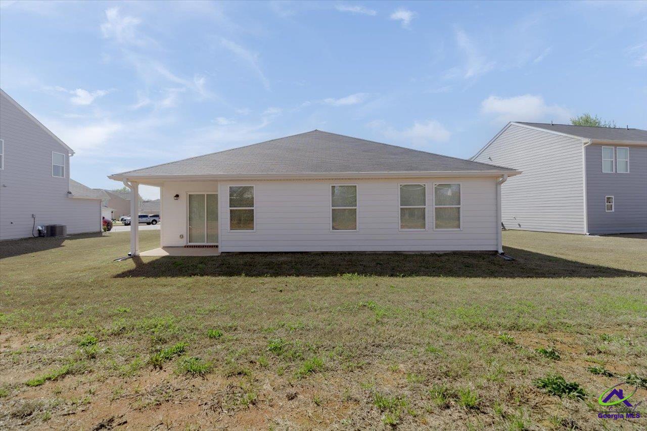 Rear of a single-story house with a covered patio, broad roof, and mostly bare lawn.