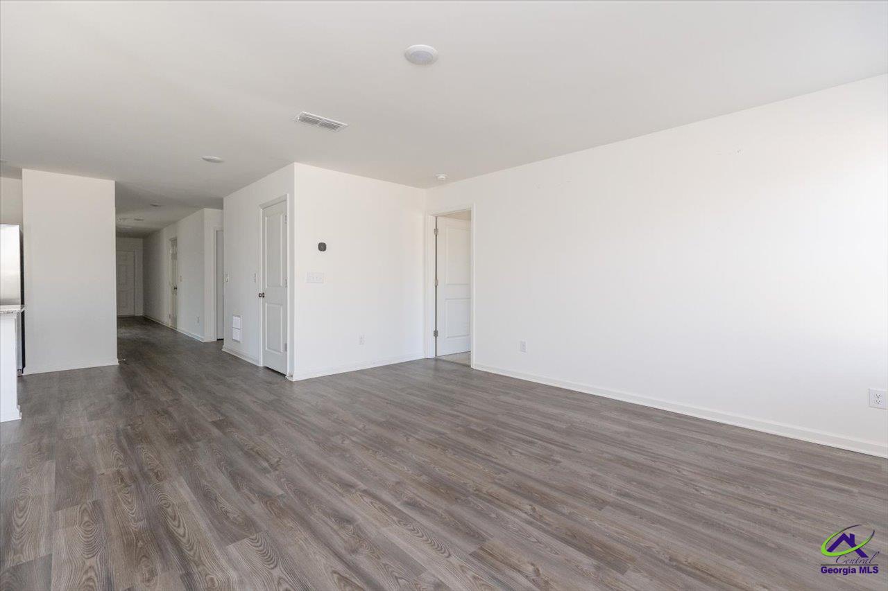 Vacant living area with gray wood-look floors and a hallway leading to several doorways.