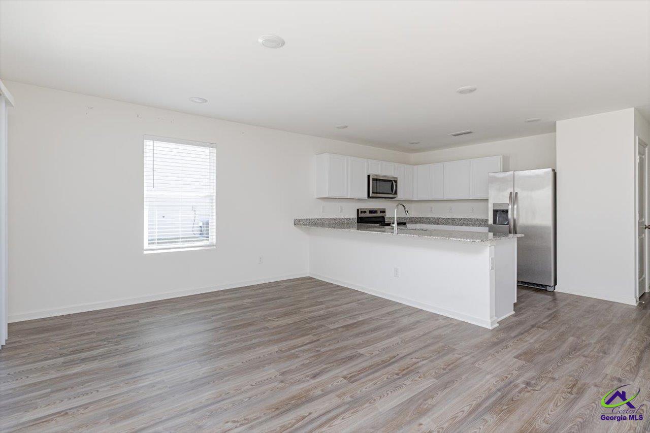 Vacant kitchen with white cabinets, granite breakfast bar, stainless steel appliances, and gray wood-look flooring.