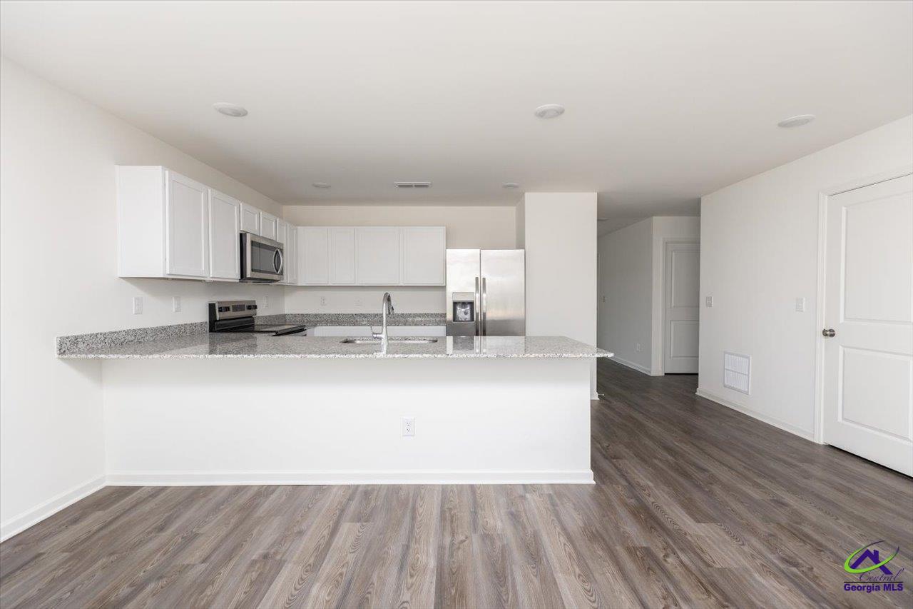 Open-plan kitchen with white cabinetry, granite counters, stainless steel appliances, and wood-look flooring.