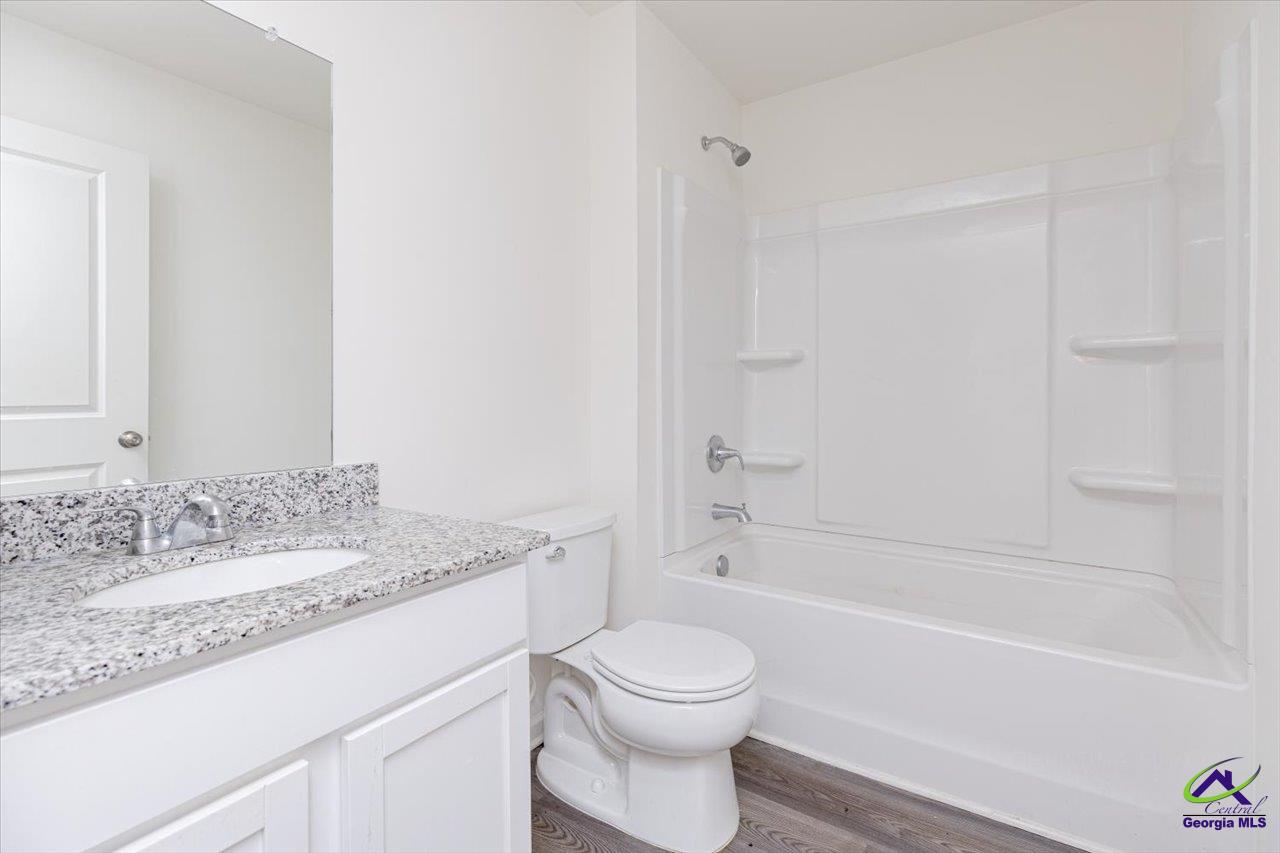 Bathroom with a white tub and shower, toilet, and granite-topped vanity.