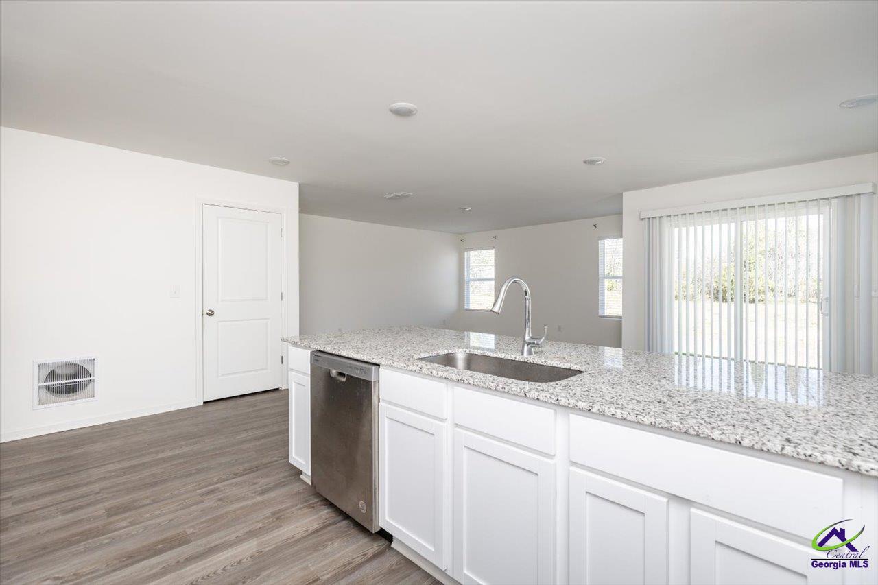 Bright vacant kitchen with a granite island, stainless dishwasher, and sliding glass doors.