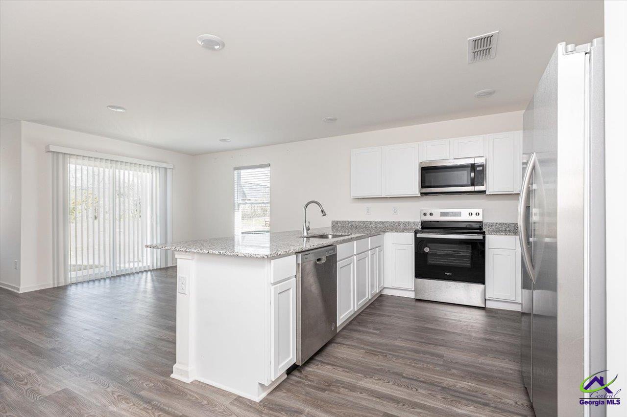 Vacant kitchen with a large granite island, white cabinets, and stainless-steel appliances.