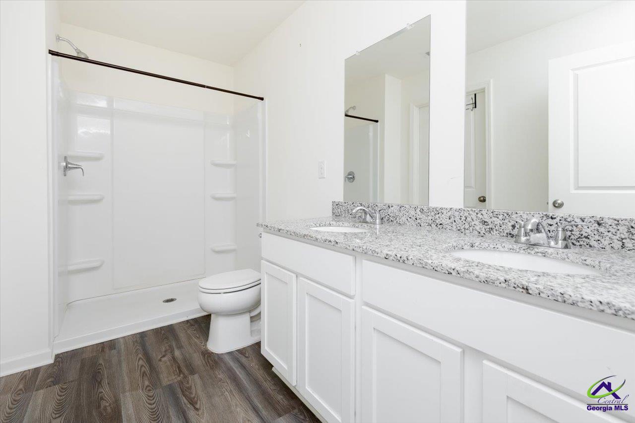 Bathroom with a white shower, toilet, and double granite-topped vanity.