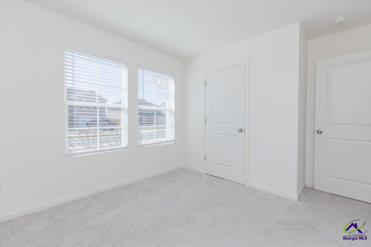 Empty carpeted room with two windows and two white doors.