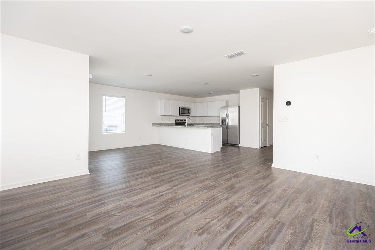 Open-plan living area with gray wood-look flooring and a white kitchen with stainless steel appliances.