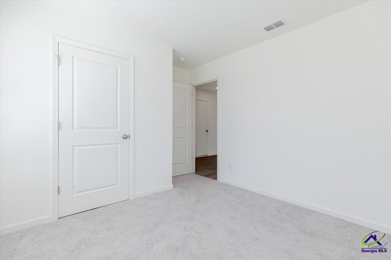 Empty carpeted room with white walls, a paneled door, and an open doorway to the hall.