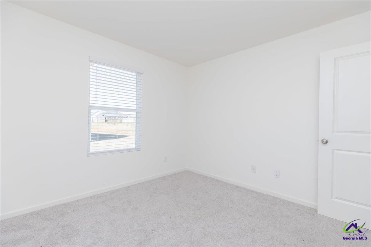 Empty carpeted room with white walls, a window with blinds, and an open door.