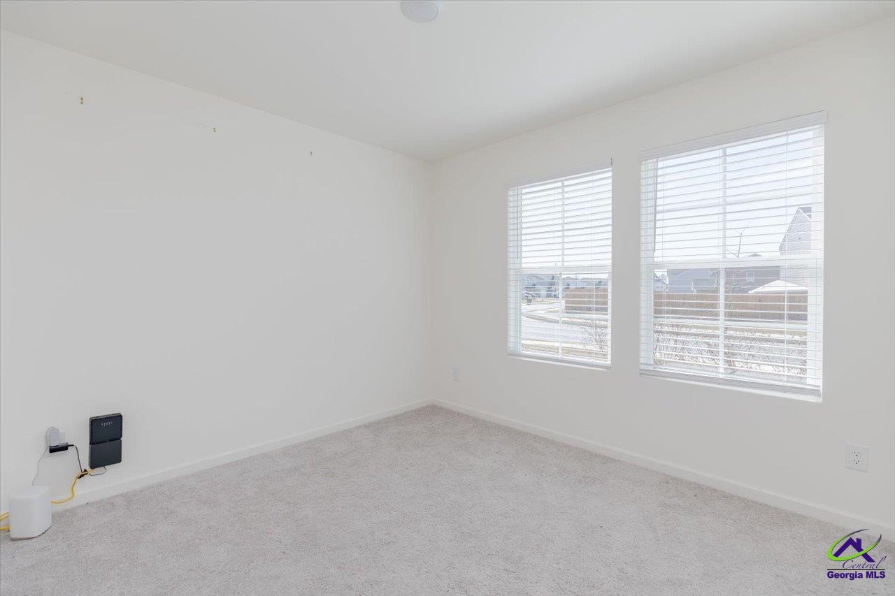Empty bedroom with light carpet and two large windows with blinds.