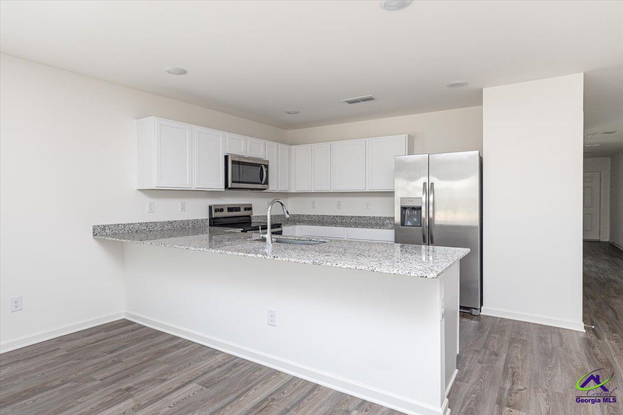 Kitchen with white cabinets, granite peninsula, stainless steel appliances, and gray wood-look flooring.