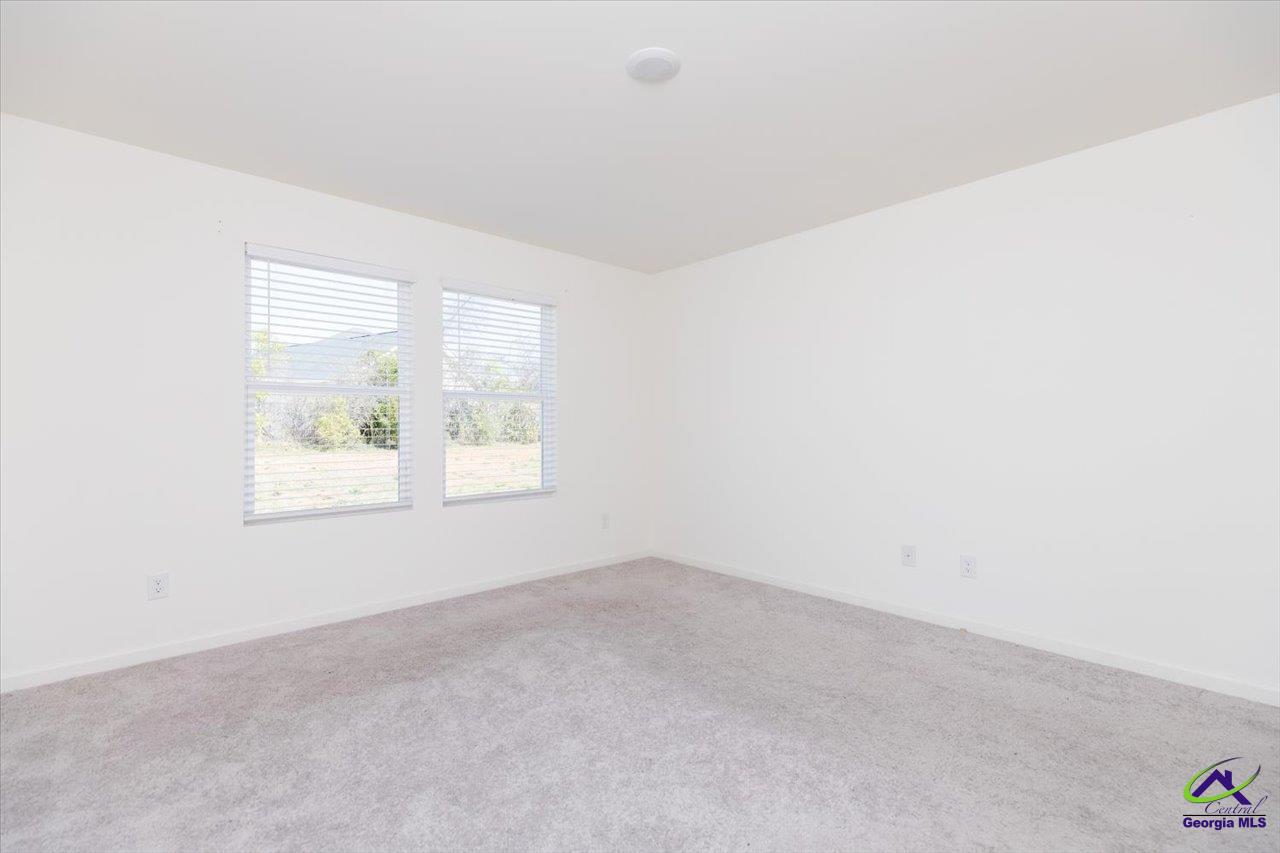 Empty carpeted room with two windows fitted with white blinds.