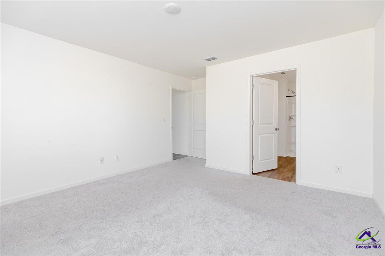 Empty bedroom with gray carpet and an open doorway to a bathroom.