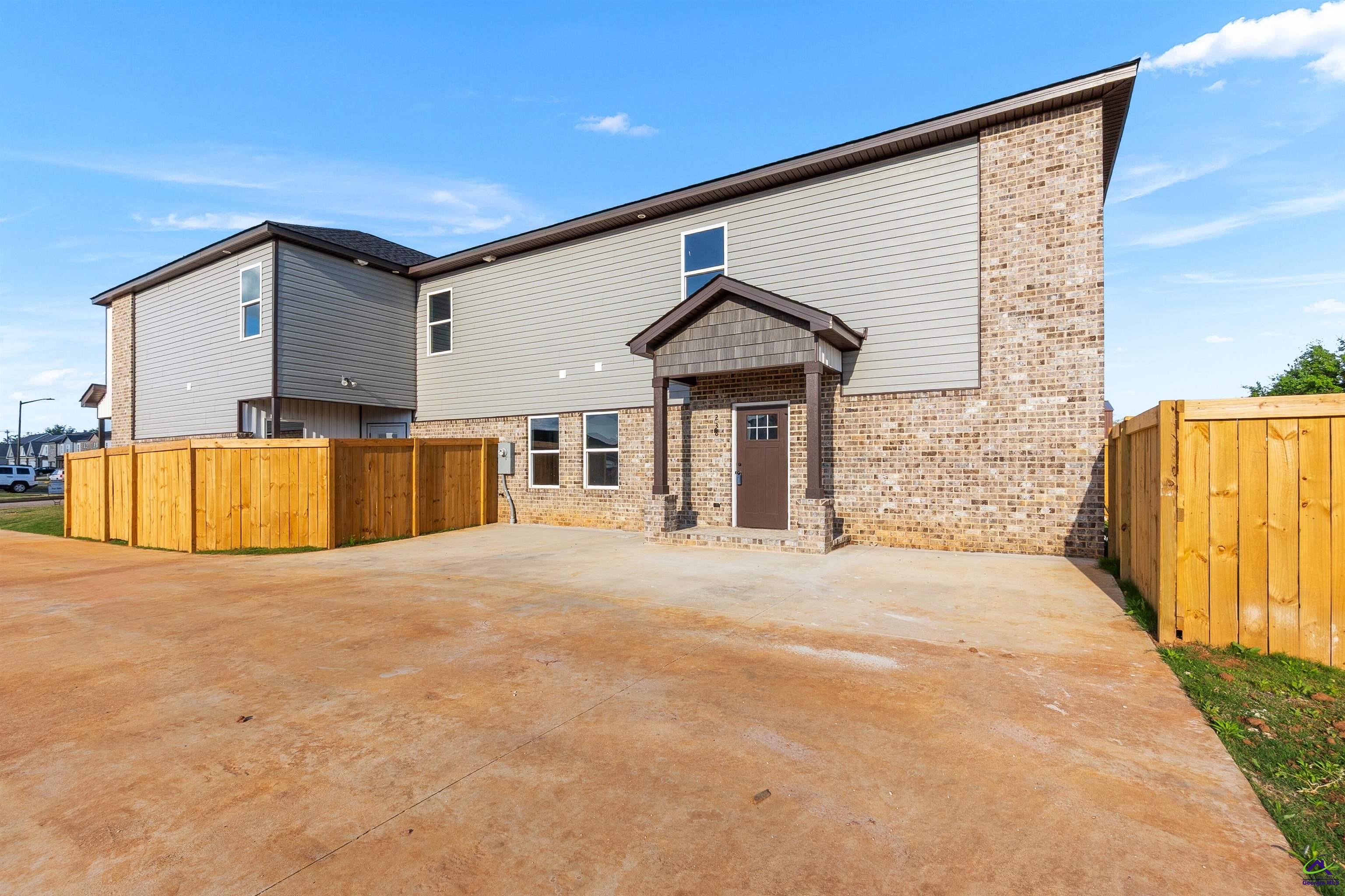 Two-story home’s rear exterior with a covered entrance, wooden privacy fence, and wide concrete patio.