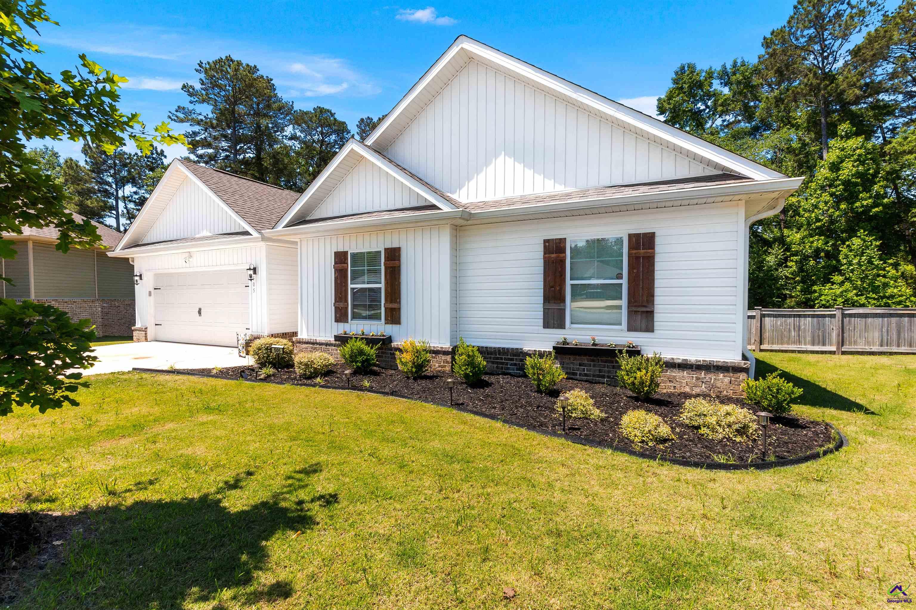 White gabled home with dark shutters, an attached garage, landscaped beds, and a broad front lawn.
