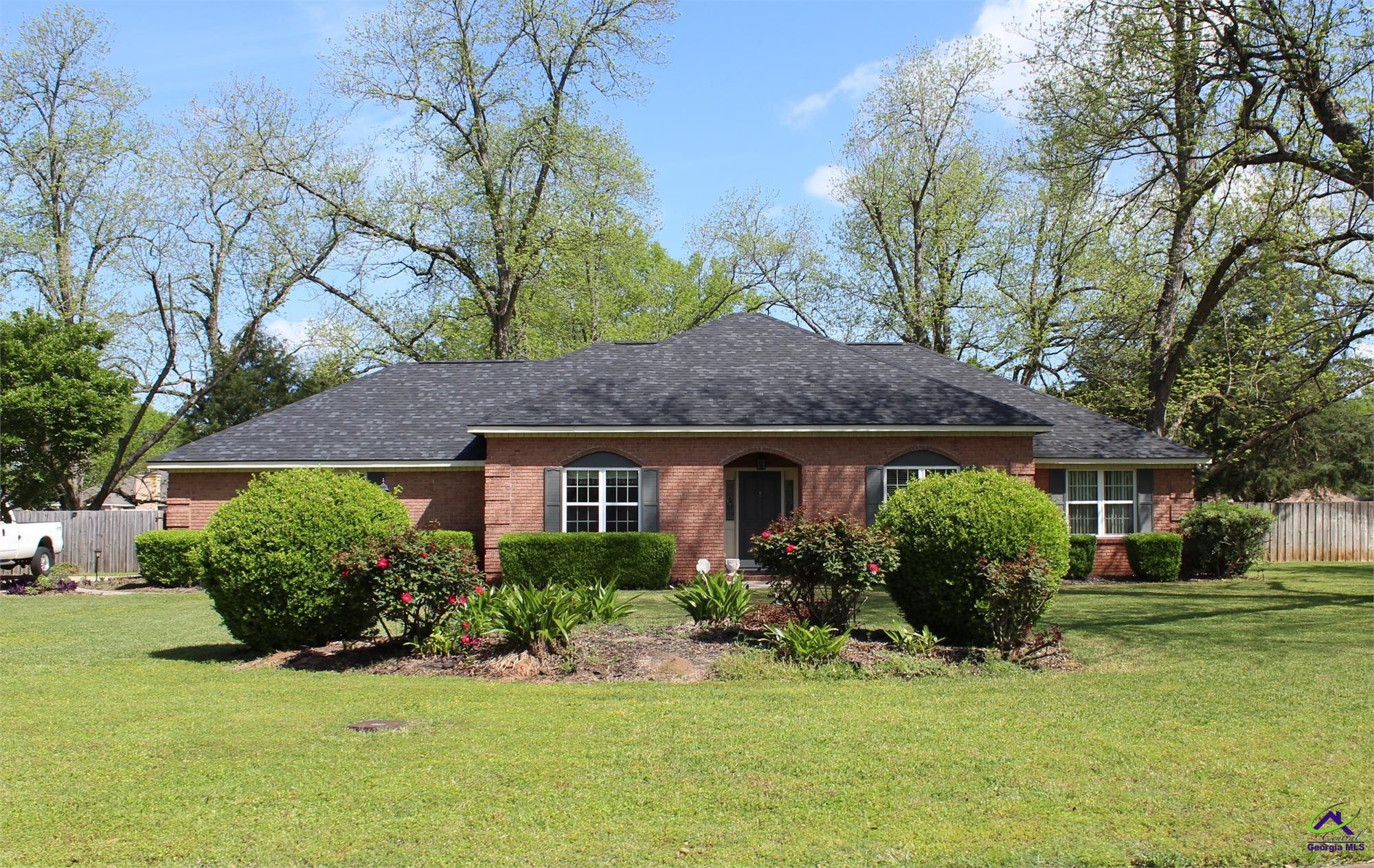 Single-story brick home with an arched entry, landscaped shrubs, and a broad green front lawn.