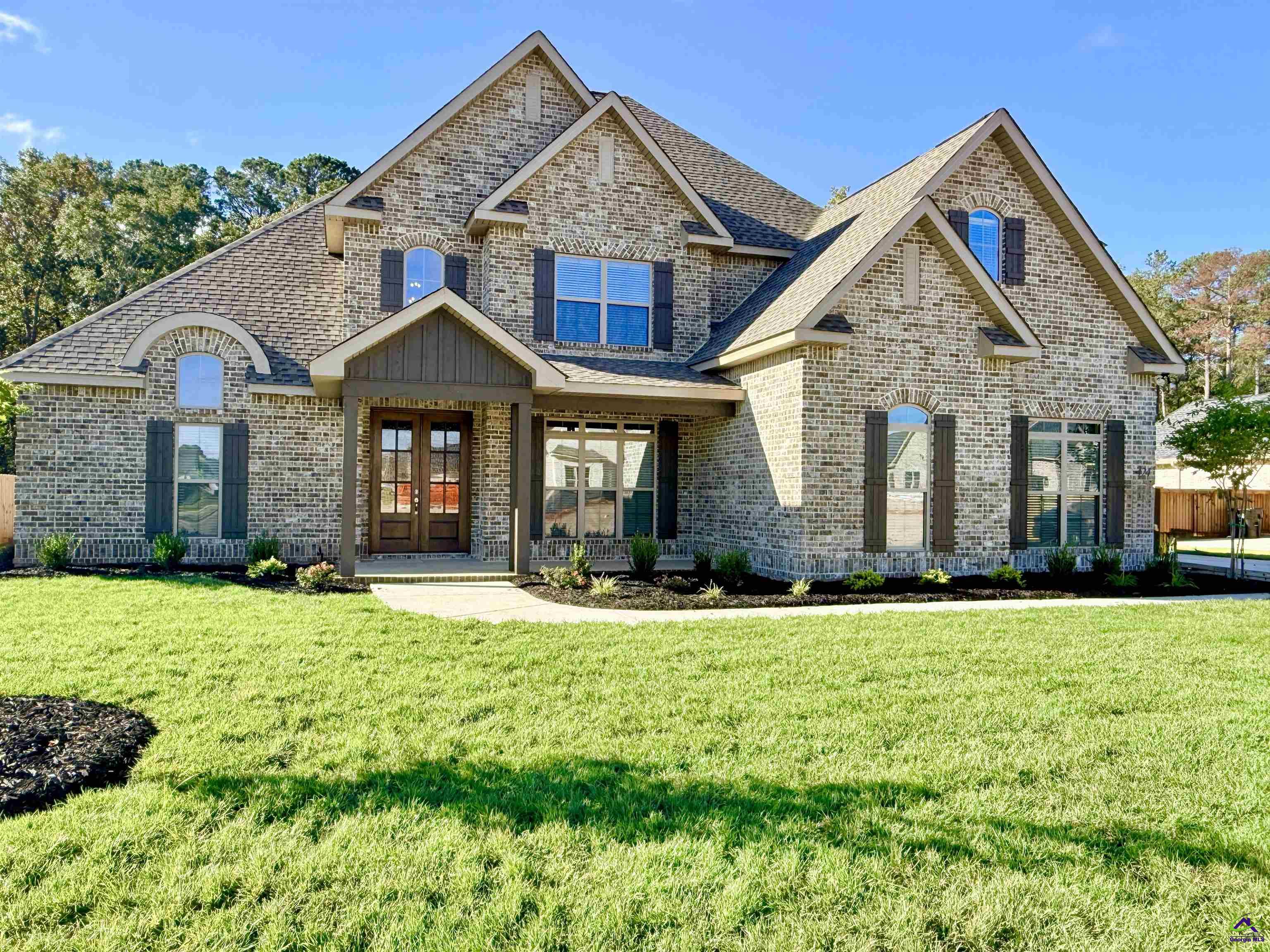 Two-story brick home with steep gables, dark shutters, and a broad green front lawn.