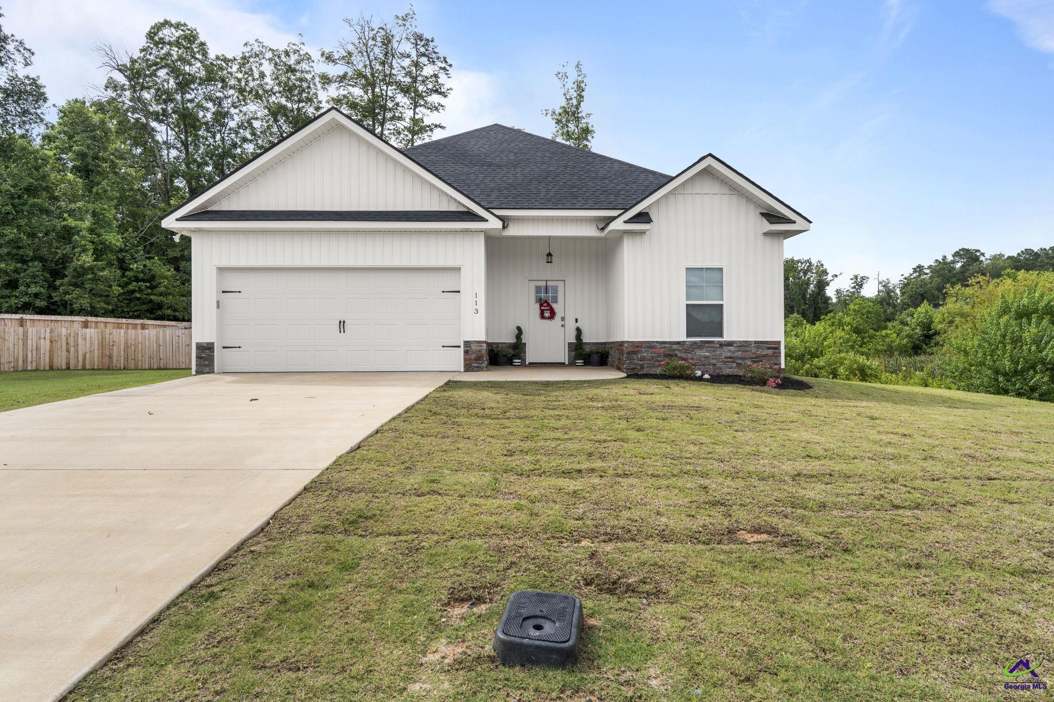 White single-story home with stone accents, an attached two-car garage, and a wide concrete driveway.