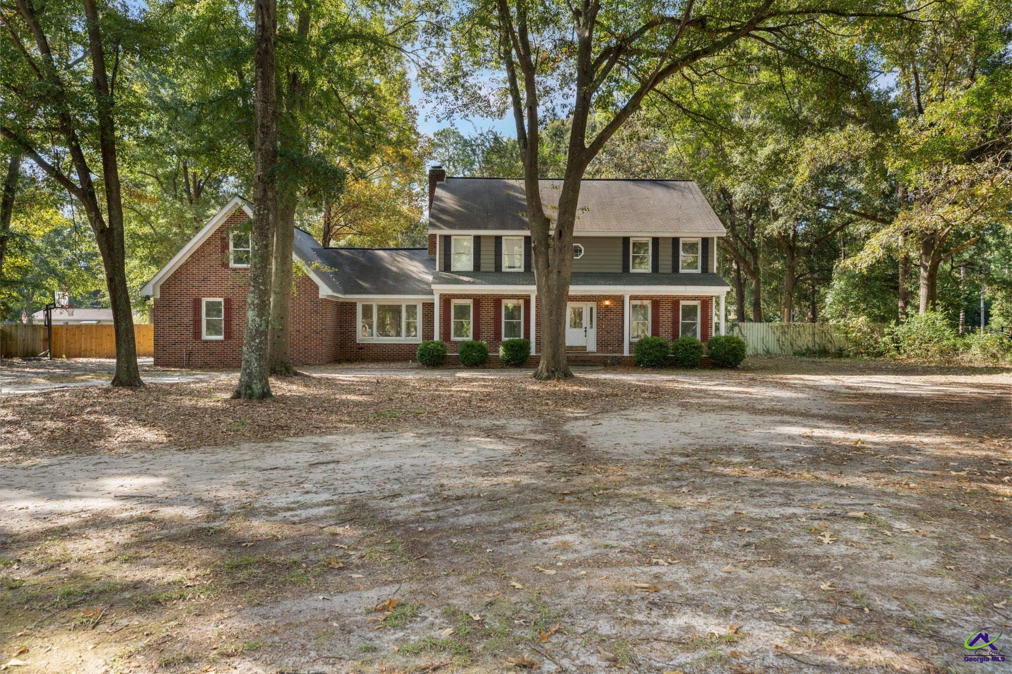 Two-story brick and gray-sided home with a covered porch among mature trees.