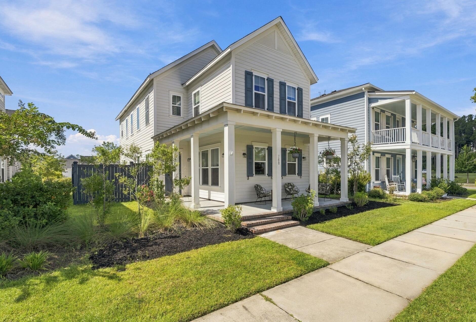 Two-story light-sided home with dark shutters, a deep covered porch, and landscaped front yard.
