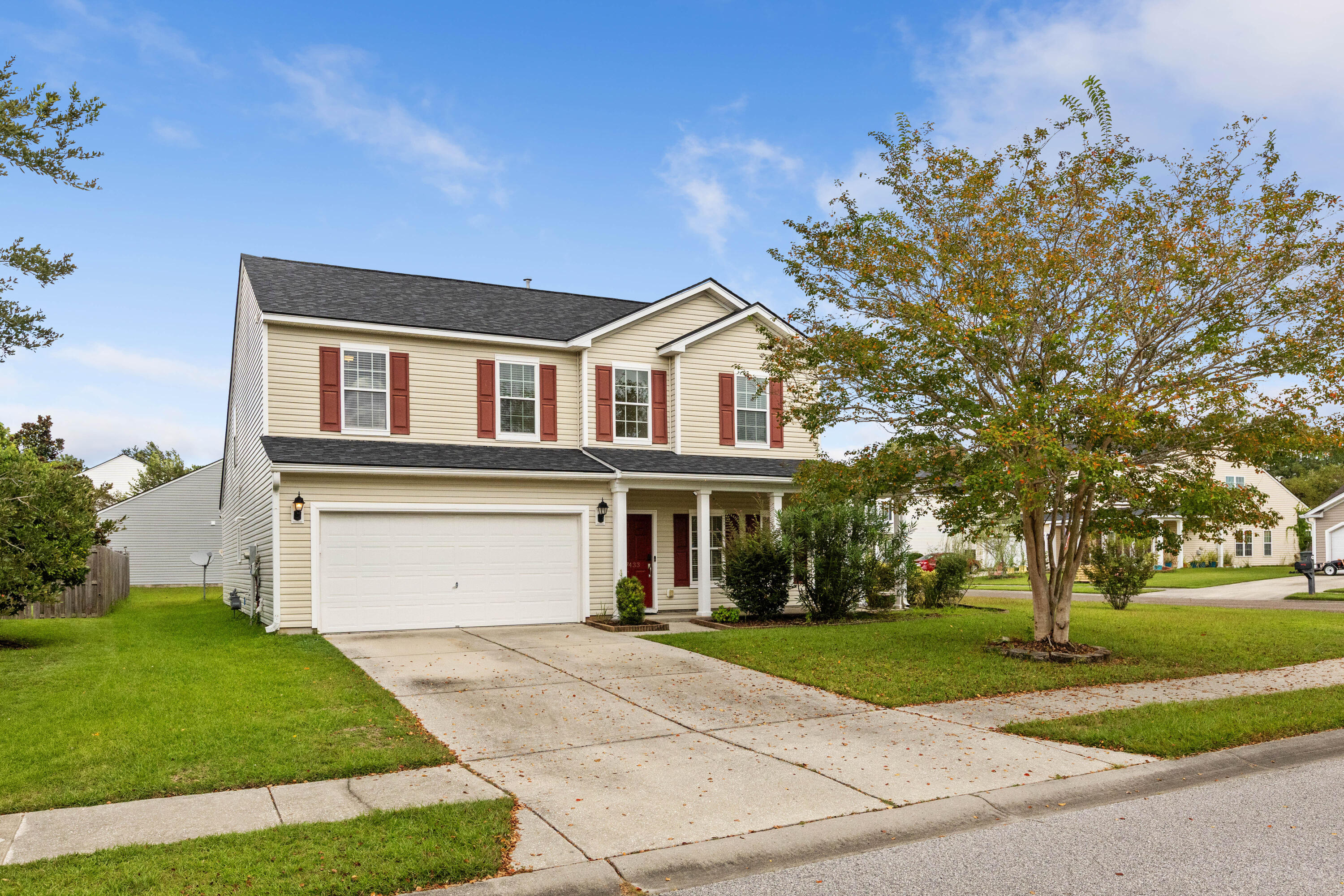 Two-story beige house with red shutters, a two-car garage, and a covered front porch.
