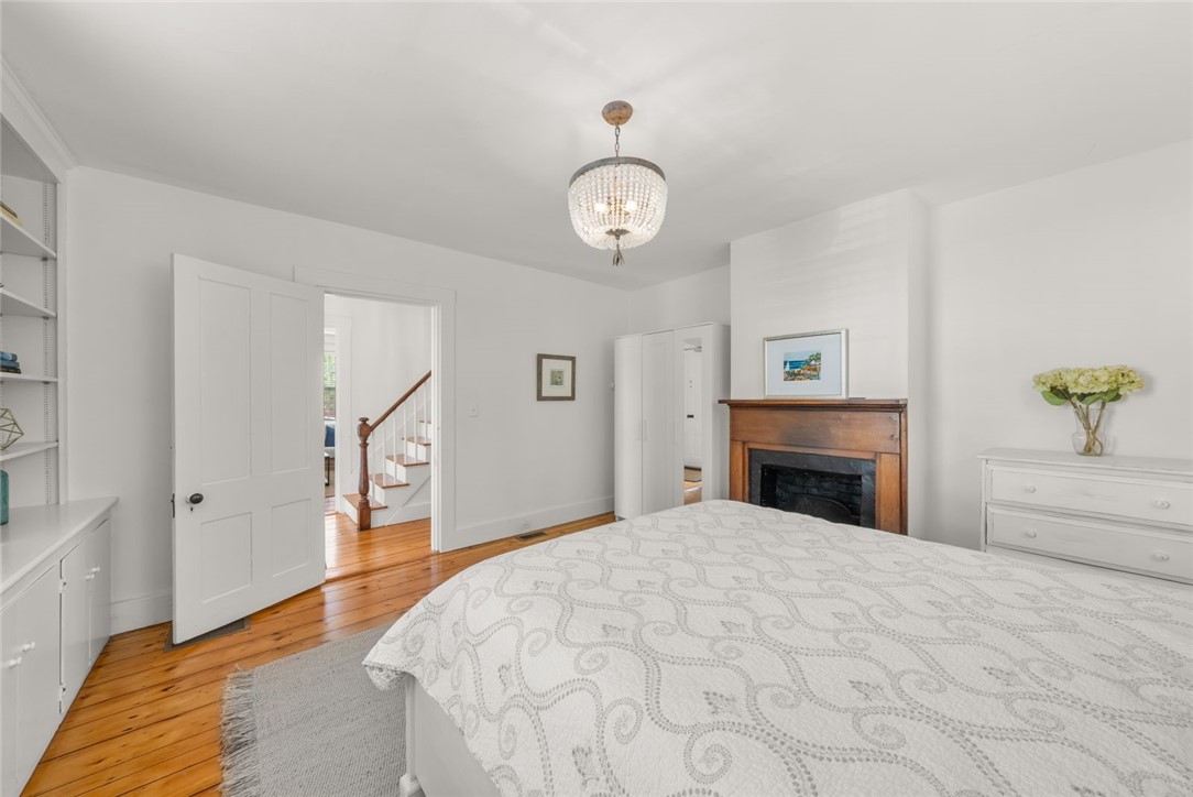 Bedroom with a patterned bed, wooden fireplace mantel, chandelier, and polished hardwood floors.